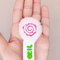 Gros plan sur la tête en doudou rose brodée du marque-page Grizzle dans une main