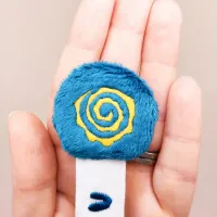 Détail de la tête du marque-page Zigwatt en minky bleu paon avec spirale jaune brodée
