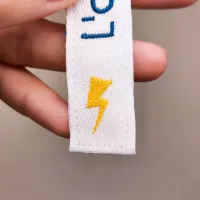 Gros plan du symbole éclair brodé sur le ruban blanc du marque-page Zigwatt